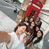 A group of students take a selfie in front of a red phone booth in England.